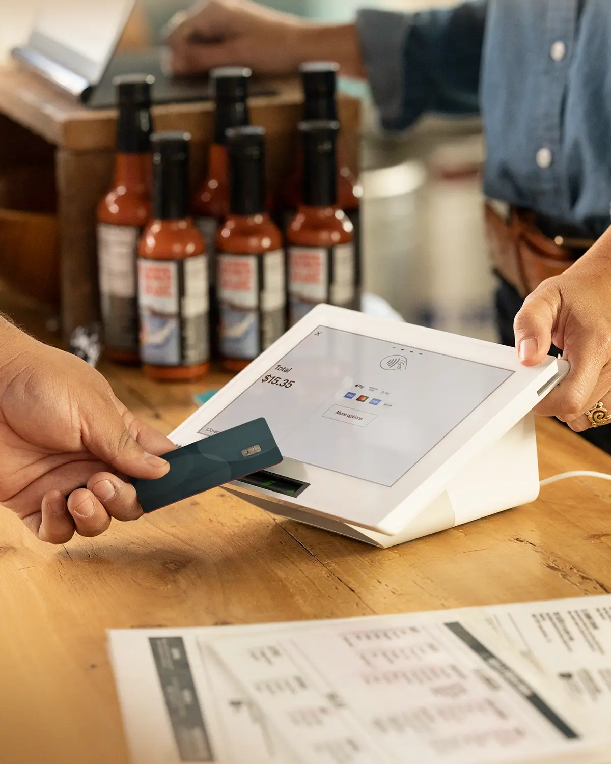 Customer tapping phone for contactless payment on Clover Mini at a bright café counter