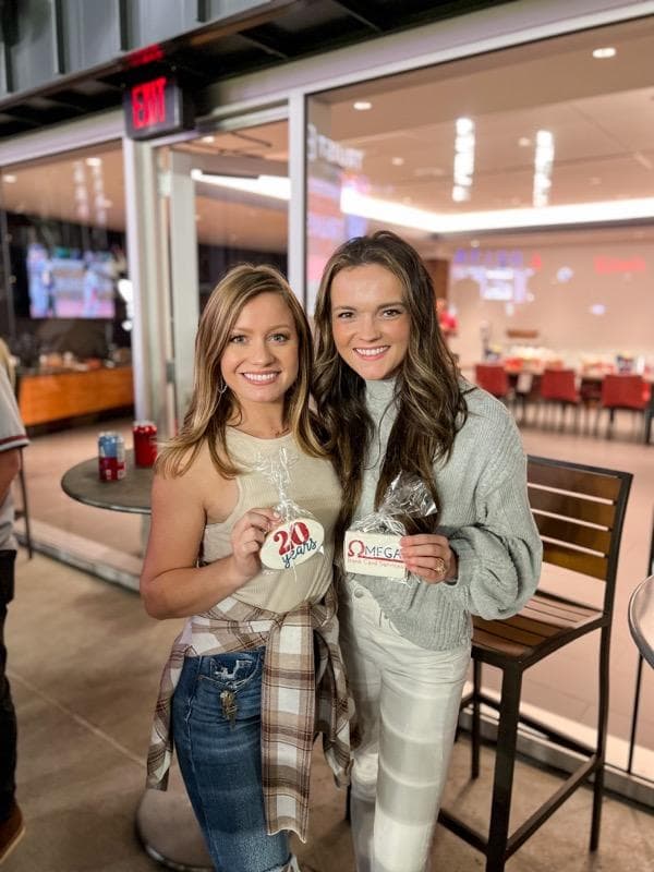 Omega team members Laura Green and Kinsey Neptune holding cookies celebrating twenty years and Omega Bank Card Services at a Braves game